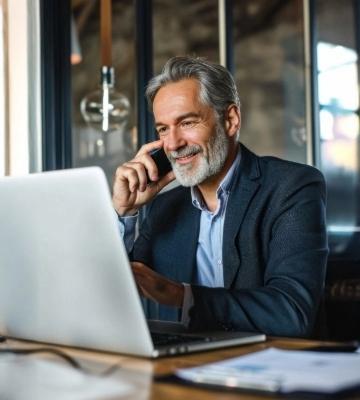 Image of a high-net-worth entrepreneur sitting at a computer taking a cell phone call.